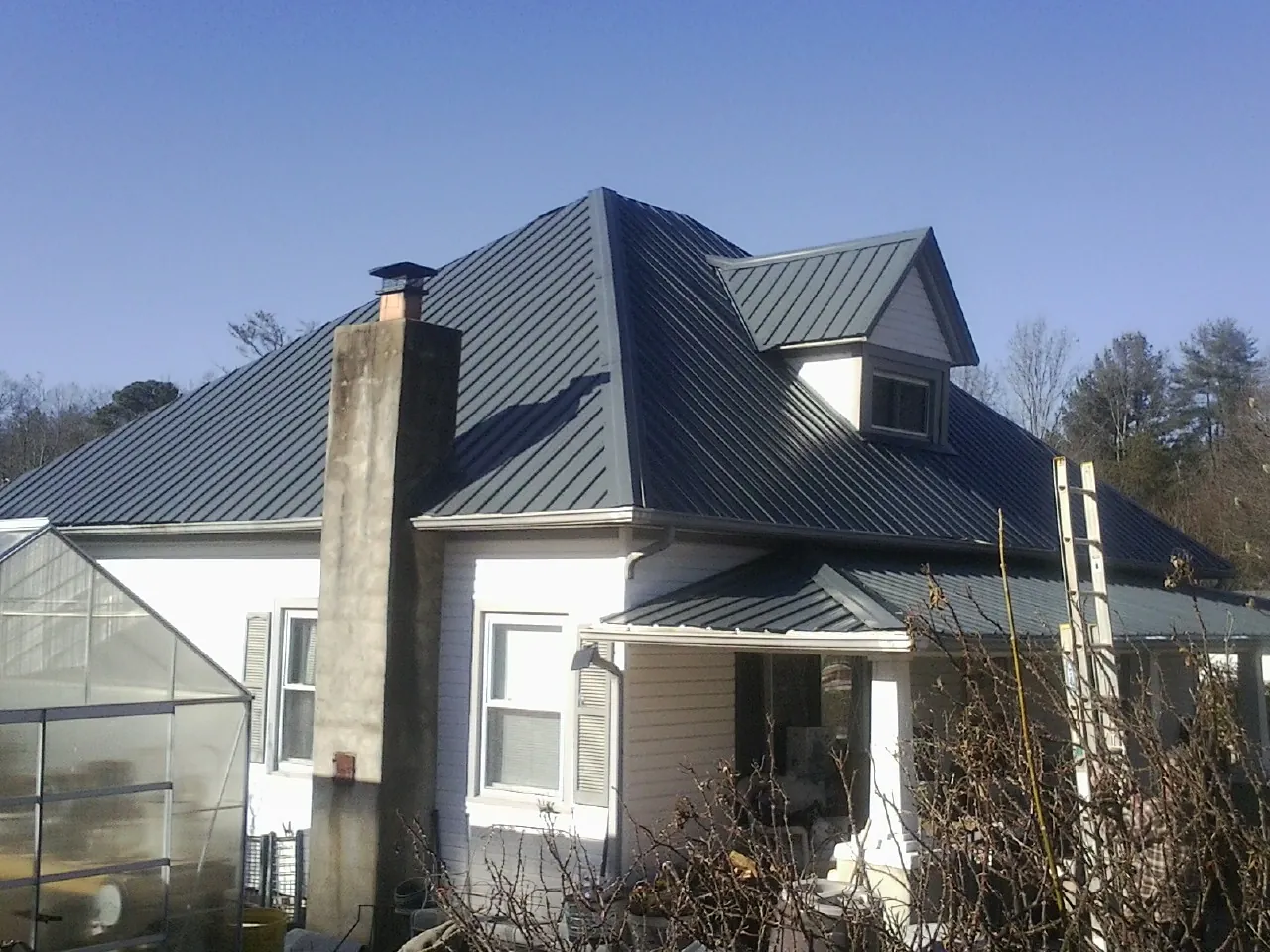 Dark blue standing seam metal roof on a white farmhouse with dormer — Slate & Tile Roof Repair by Roofing Brothers in Hordville