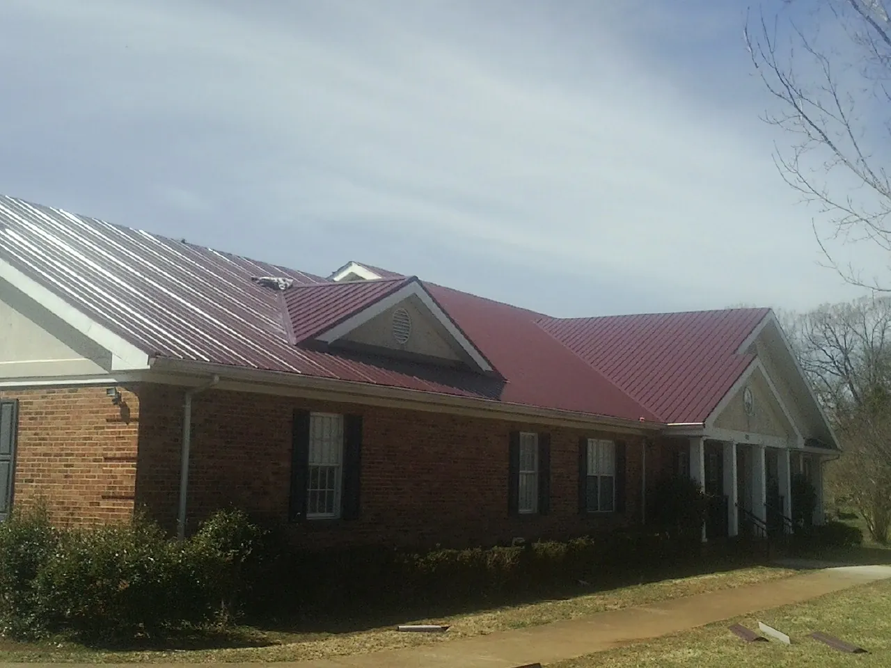 Red metal roof with gabled entries on a long brick building, from a Hail Damage Roof Repair job in Hordville