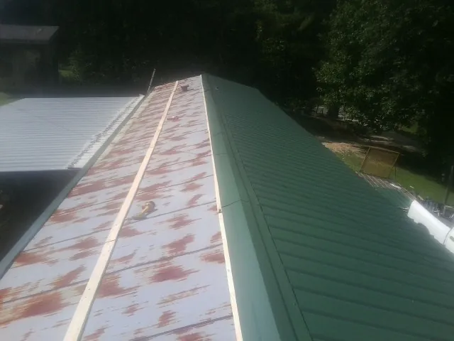 Old rusted panels beside newly installed green metal roofing — Wind Damage Roof Repair by Roofing Brothers in Hordville