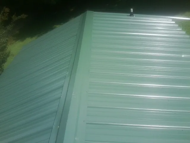 New green metal panels meeting at the ridge of a roof — Flat Roof Repair work by our crew in Hordville