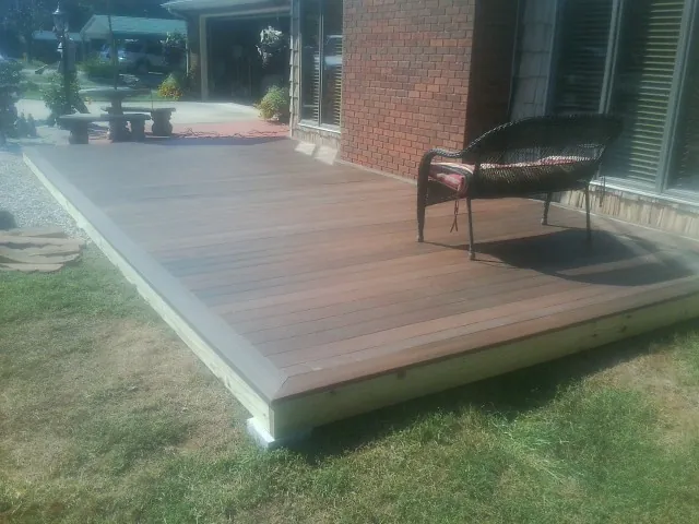 New wood deck and wicker chair beside a brick house in Hordville
