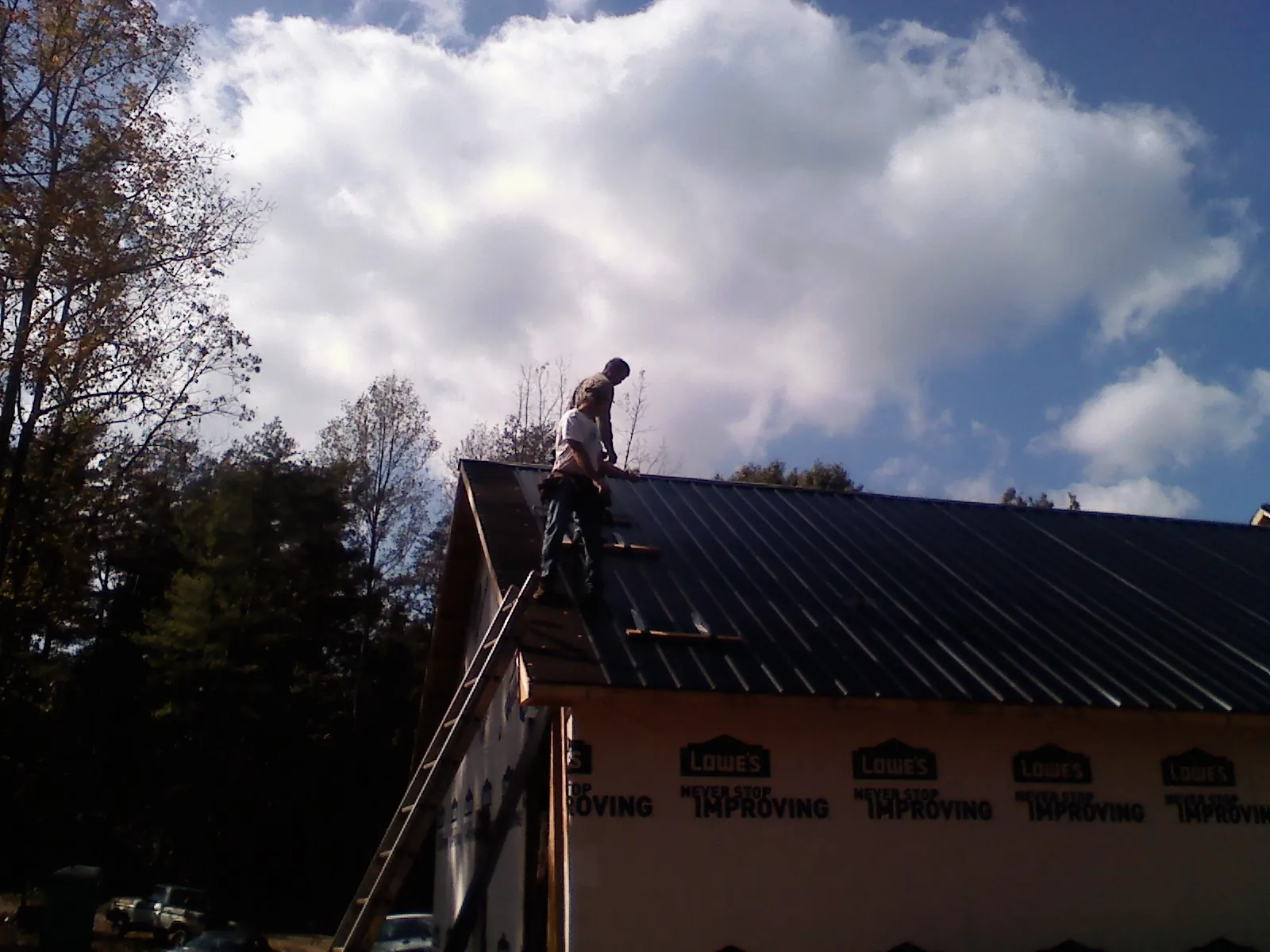 Roofer fastening dark metal panels high against a cloudy sky, from a Roof Inspection job in Hordville