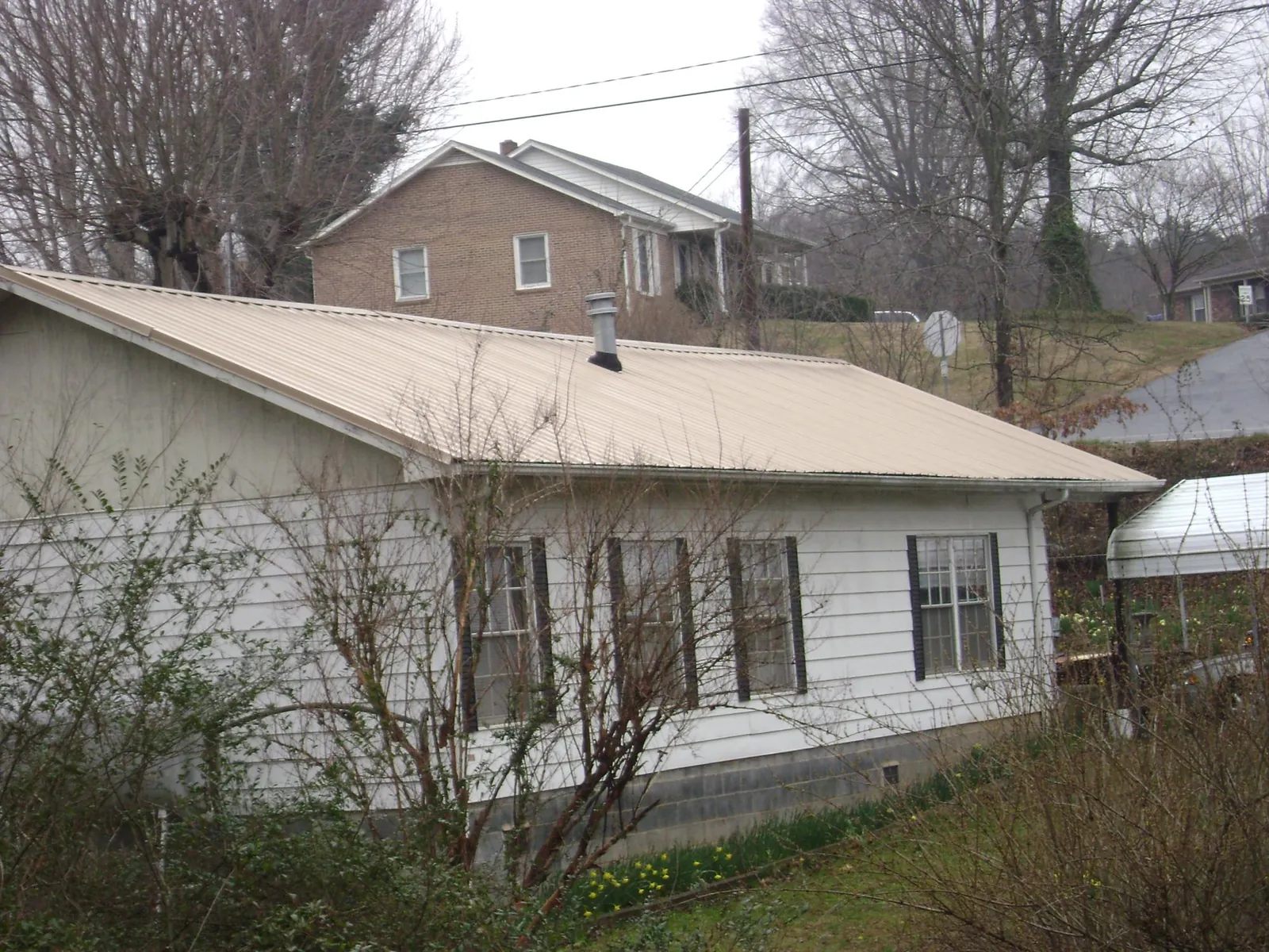 Tan metal roof on a white sided house set into a hillside — Commercial Roofing by Roofing Brothers in Hordville